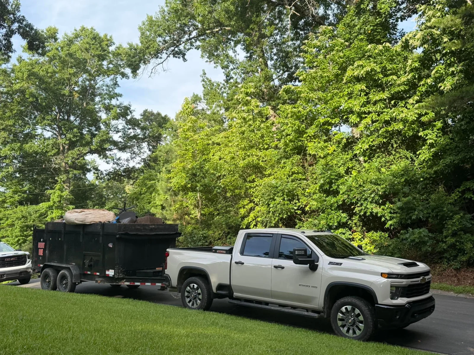 A white pickup towing a black dump trailer loaded with bulky items